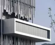 The gallery's protruding structure cuts across the facade, which is composed of vertical aluminum elements resembling a silvery reed bed