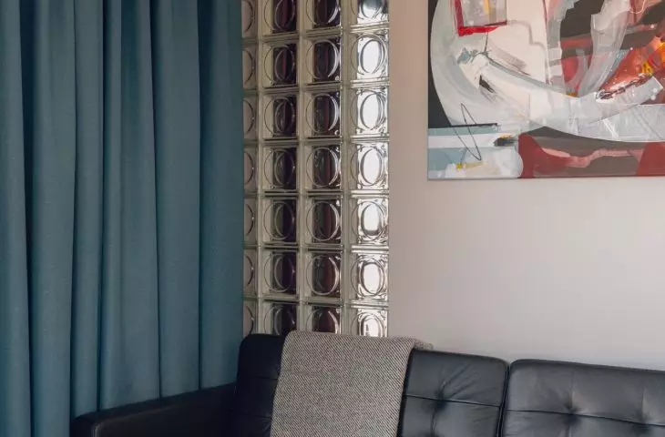 The leather sofa is paired with a painting by Emilia Kohut and a wall made of glass blocks, through which light enters the bedroom