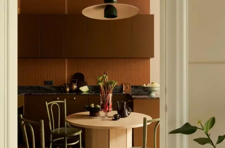 The brick-red ceiling defines the kitchen, and vintage green chairs surround the oak table