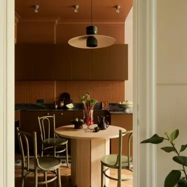 The brick-red ceiling defines the kitchen, and vintage green chairs surround the oak table