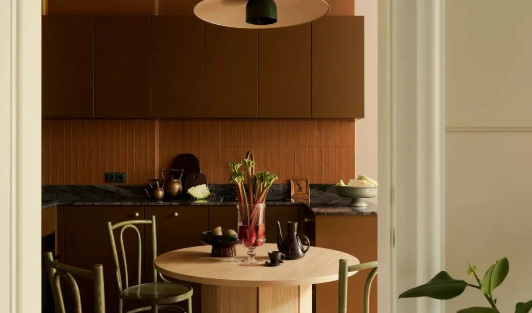 The brick-red ceiling defines the kitchen, and vintage green chairs surround the oak table