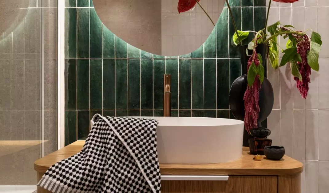 Dark green tiles and a lighted mirror give this small bathroom a distinctive character