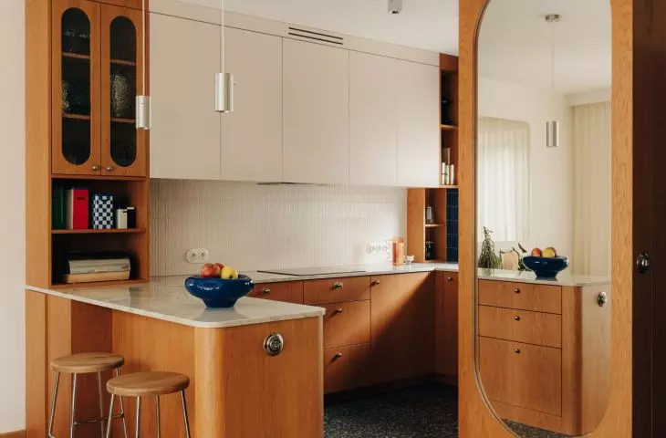 The veneered kitchen cabinets are complemented by stone countertops, terrazzo tiles, and chrome accents