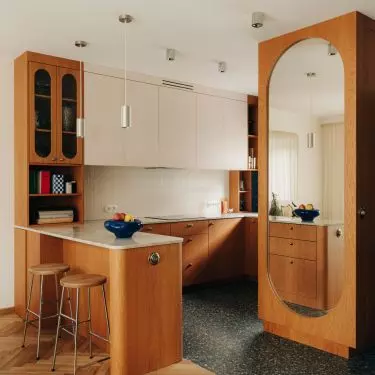 The veneered kitchen cabinets are complemented by stone countertops, terrazzo tiles, and chrome accents