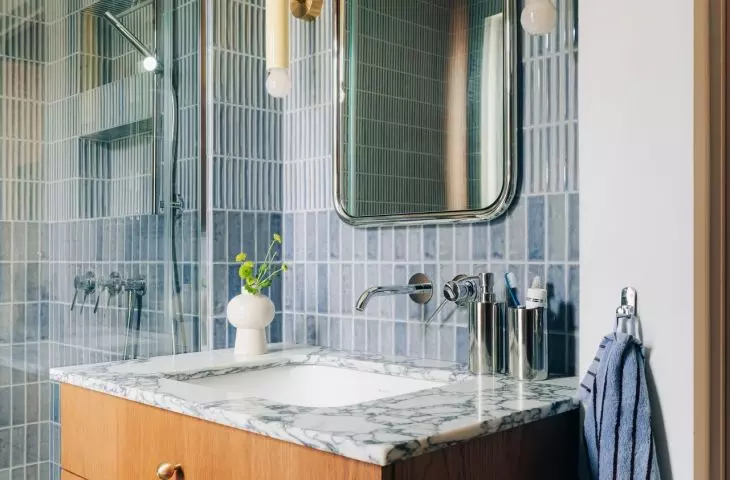 The blue tiles in the bathroom are paired with warm wood veneer, stone, and chrome