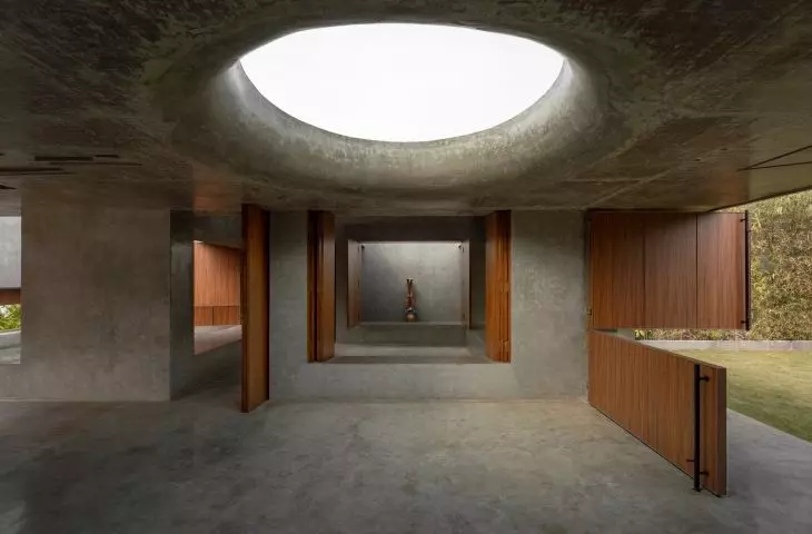An oval skylight illuminates the center of the concrete interior, and wooden panels open it up to the garden