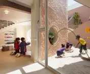 The large glass walls blur the line between the classroom and the outdoor area with a sandbox 