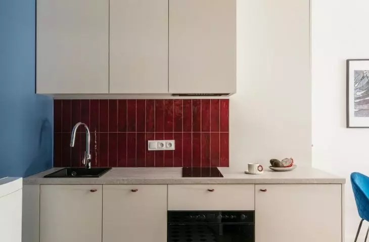 The kitchenette features a cobalt-blue wall that extends up to the ceiling and burgundy tiles above the countertop