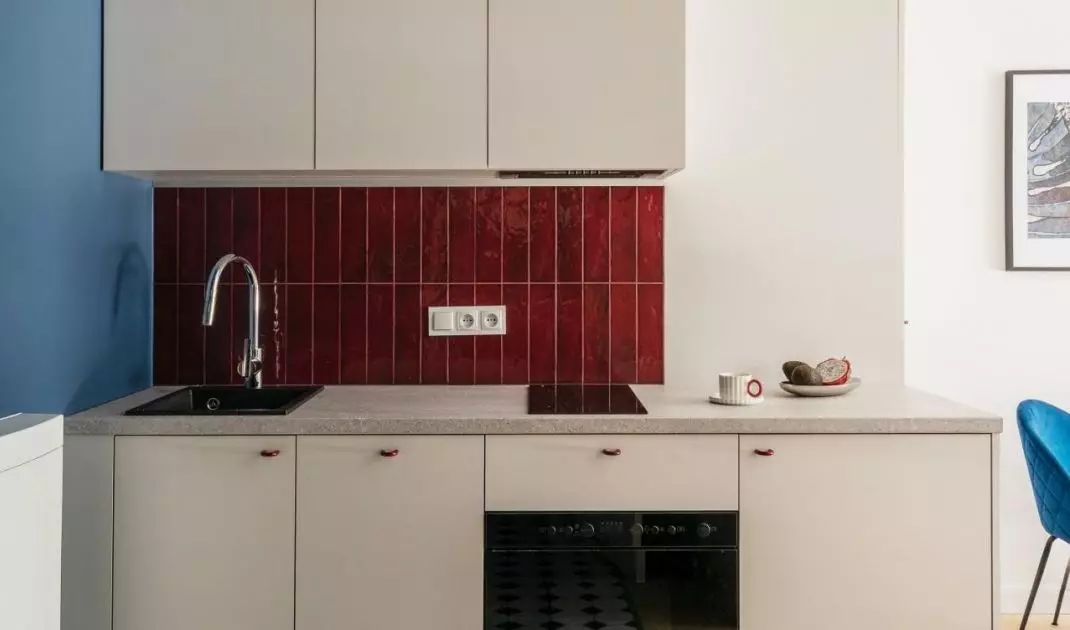 Aneks kuchenny wyróżniają kobaltowa ściana przechodząca na sufit oraz burgundowe płytki nad blatem