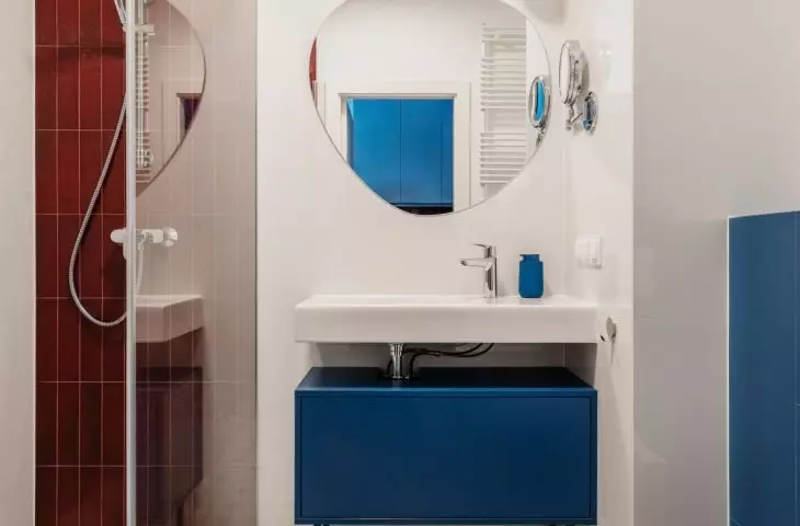 The apartment's color scheme is echoed in the bathroom with burgundy tiles and a blue cabinet under the sink