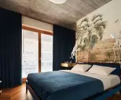 behind the headrest of the bed there is a colorful wallpaper with a rainforest pattern and monkey-shaped bedside lamps