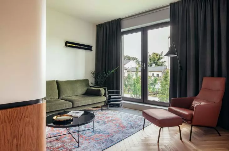 zielona, sztruksowa sofa, skórzany fotel, kolorowy dywan i stylowy gazetnik z lat 70. urozmaicają salon