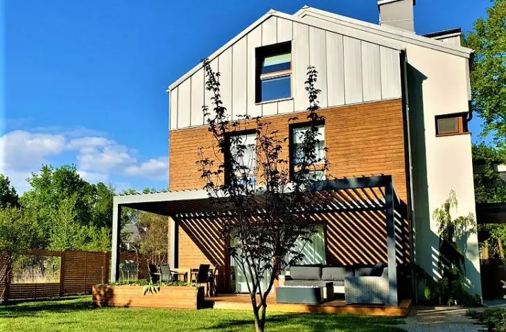 Pergola mocowana na czterech słupach, przylegająca do ściany budynku