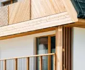 Walls covered with plaster in a shade of warm white correspond with wooden elements of the facade